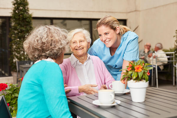 Fachkraft für Pflegeassistenz redet mit zwei Patientinnen