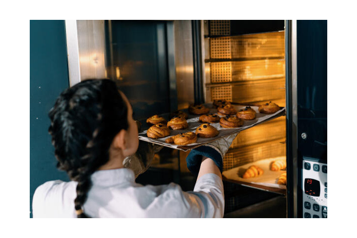 Bäckereifachverkäuferin nimmt Blech aus dem Ofen