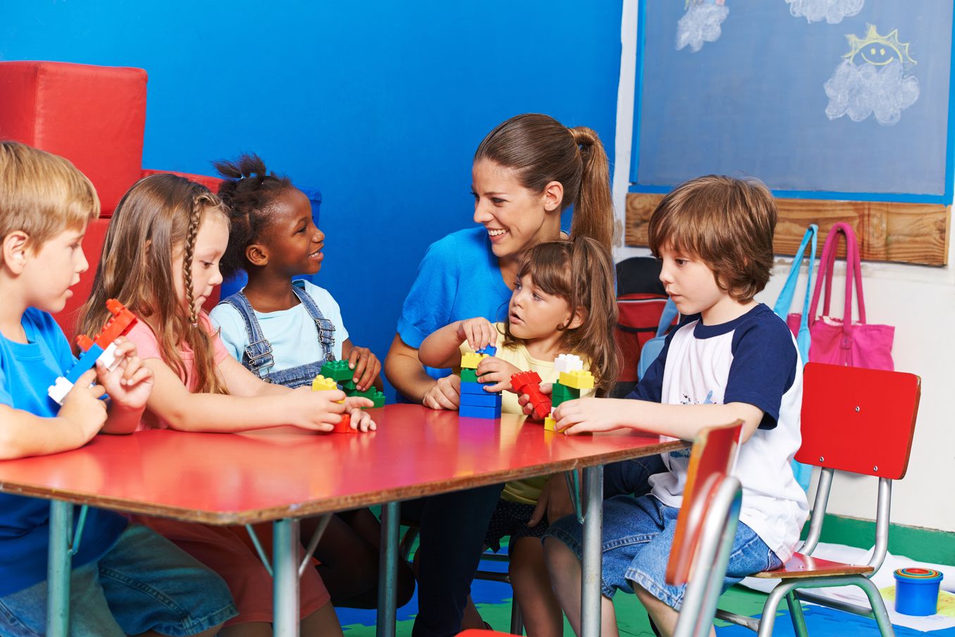 Erzieher Studium – Erzieherin spielt mit fuenf Kindern an einem Tisch