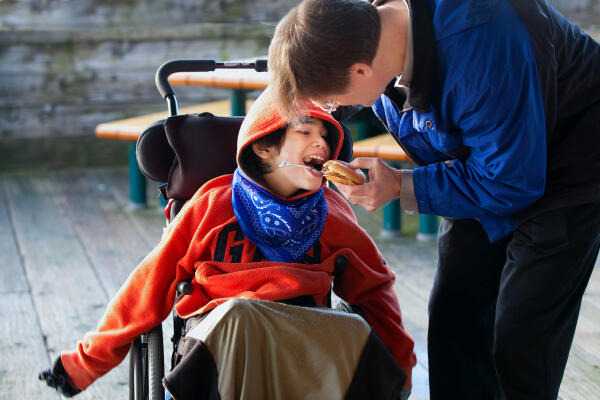 Heilerziehungspfleger füttert Kind im Rollstuhl