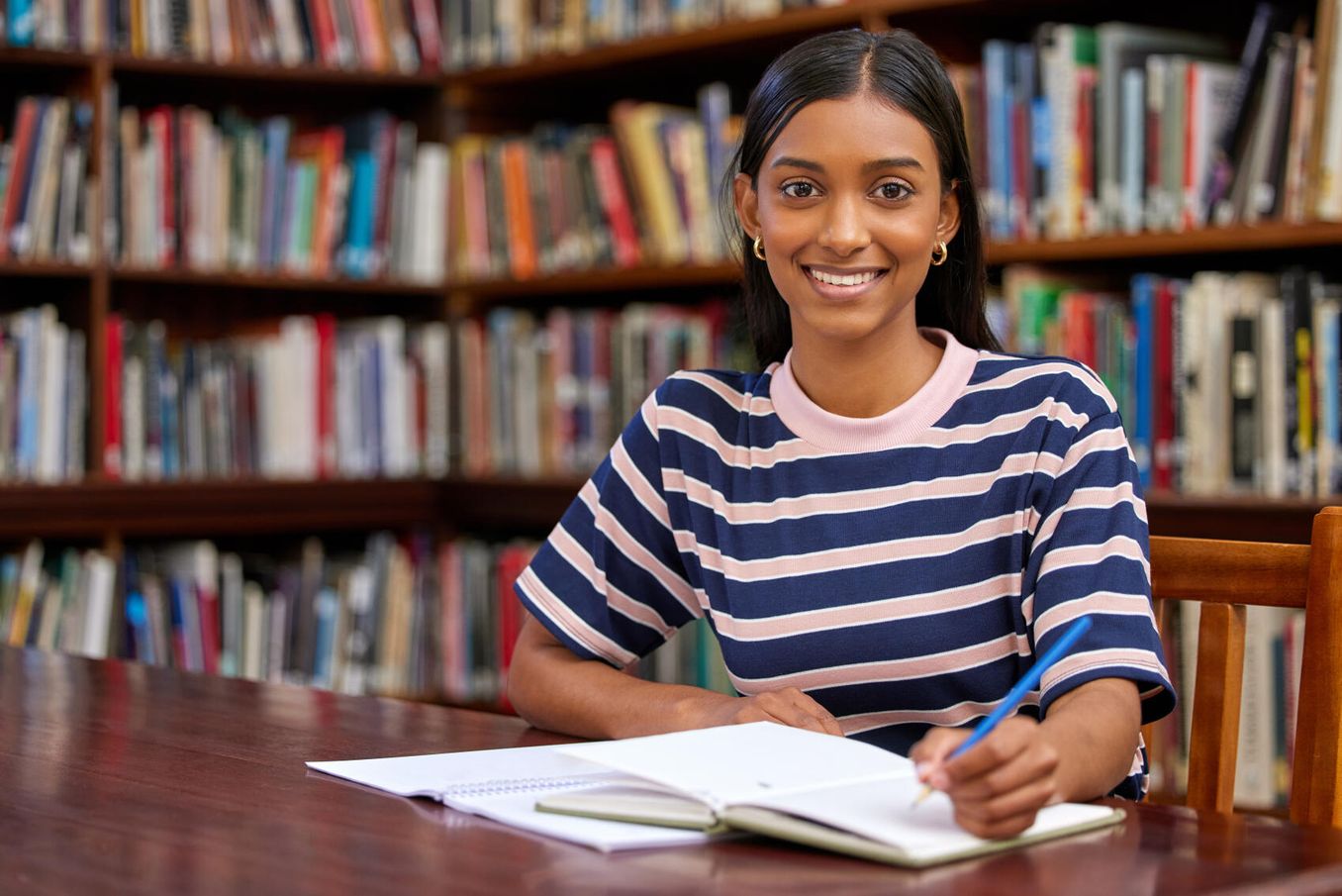 Semesterstart – fröhliche Studentin lernt in Bibliothek