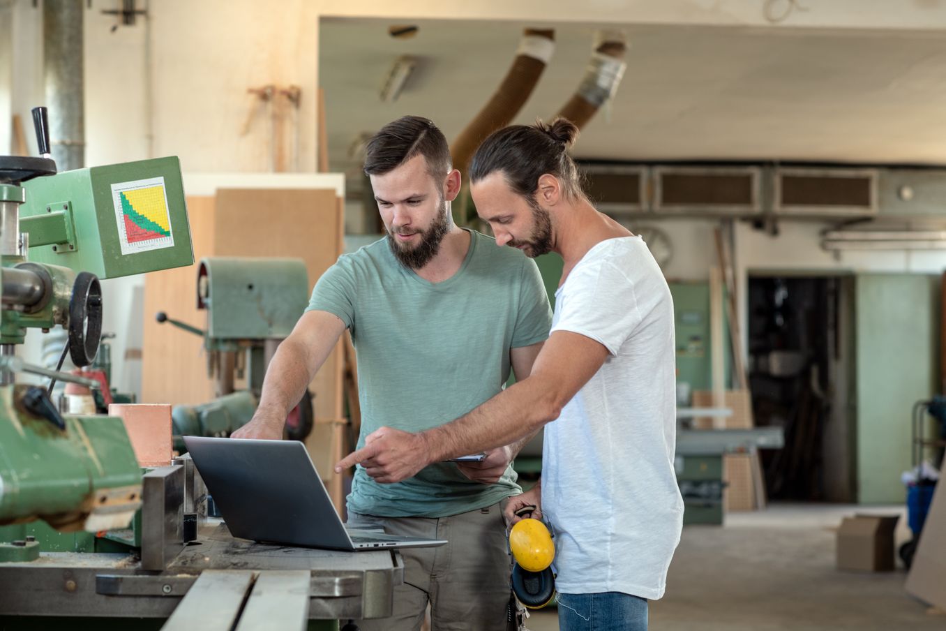 Holztechnik Studium – zwei Holztechniker zeigen auf einen Laptop an einer Maschine