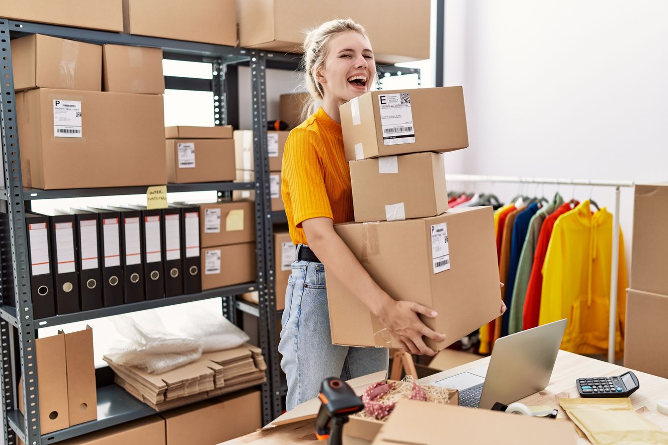 Handelsmanagement Studium – Studentin traegt drei Pakete aus dem Lager und lacht