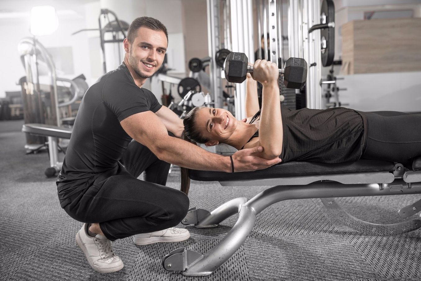 Sportmanagement Studium – Trainer unterstuetzt eine Sportlerin mit Hanteln