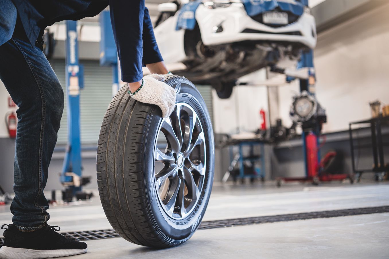 Fahrzeugtechnik Studium – Mann rollt einen Autoreifen durch eine Werkstatt
