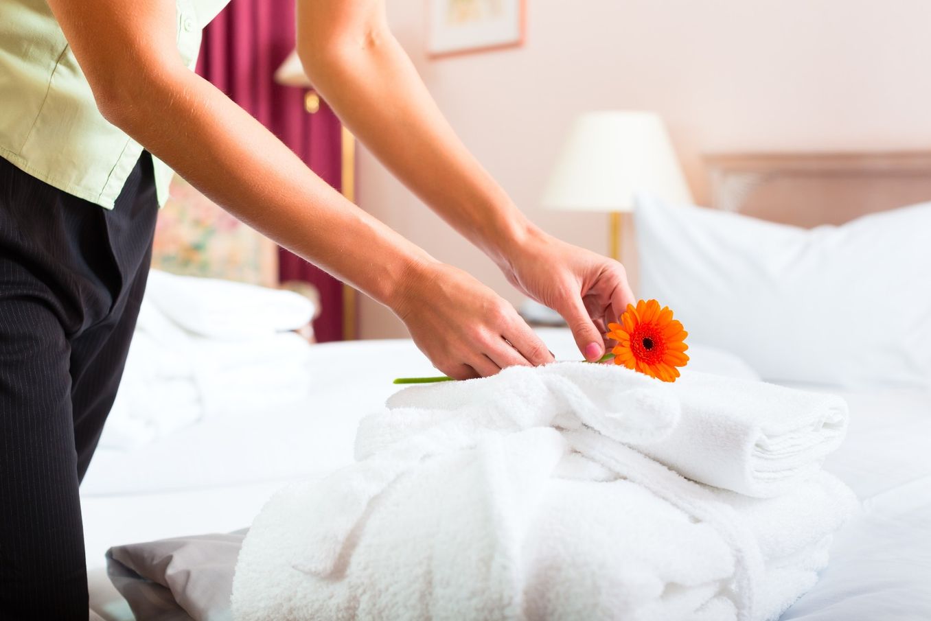 Hotelmanagement Studium – Frau platziert eine Blume auf frisch gemachtem Bett