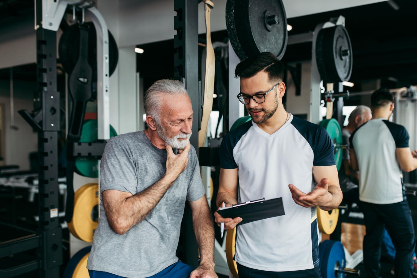 Fitnesstraining Studium – Fitnesstrainer erklaert Kunden Trainingsplan