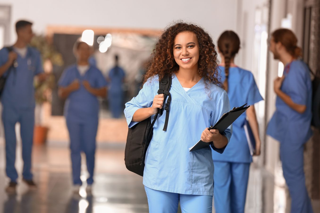Gesundheit Studium – Studentin in Kasack traegt ein Klemmbrett und laechelt