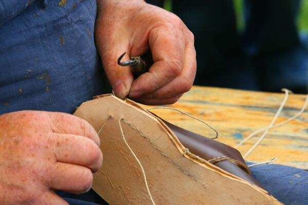 Maßschuhmacher näht Sohle an Maßschuhmacher näht Sohle an