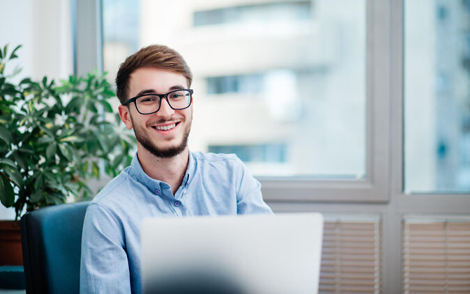 Werkstudent lächelt am Laptop im Büro Werkstudent laechelt am Laptop im Buero
