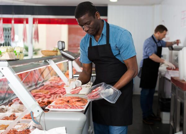 Fachverkaeufer im Lebensmittelhandwerk packt Fleisch ab