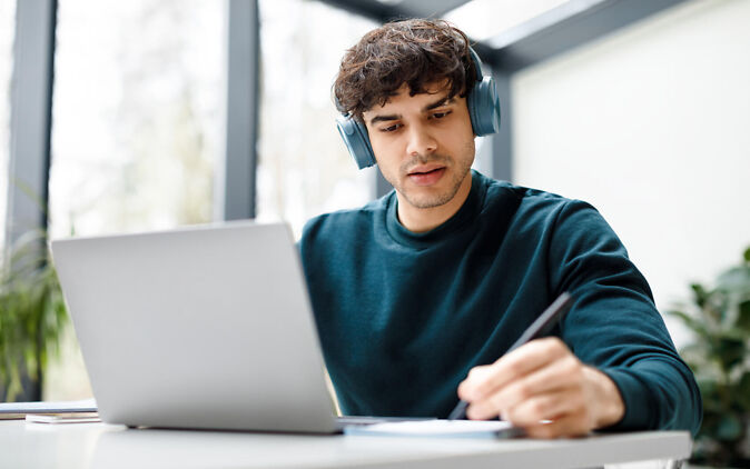 Student mit Kopfhörern schreibt Seminararbeit am Laptop Student mit Kopfhoerern schreibt Seminararbeit am Laptop