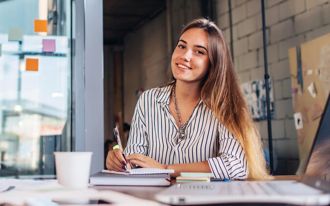 Berufe mit Abitur – Junge Frau sitzt lächelnd an Schreibtisch Berufe mit Abitur – Junge Frau sitzt laechelnd an Schreibtisch